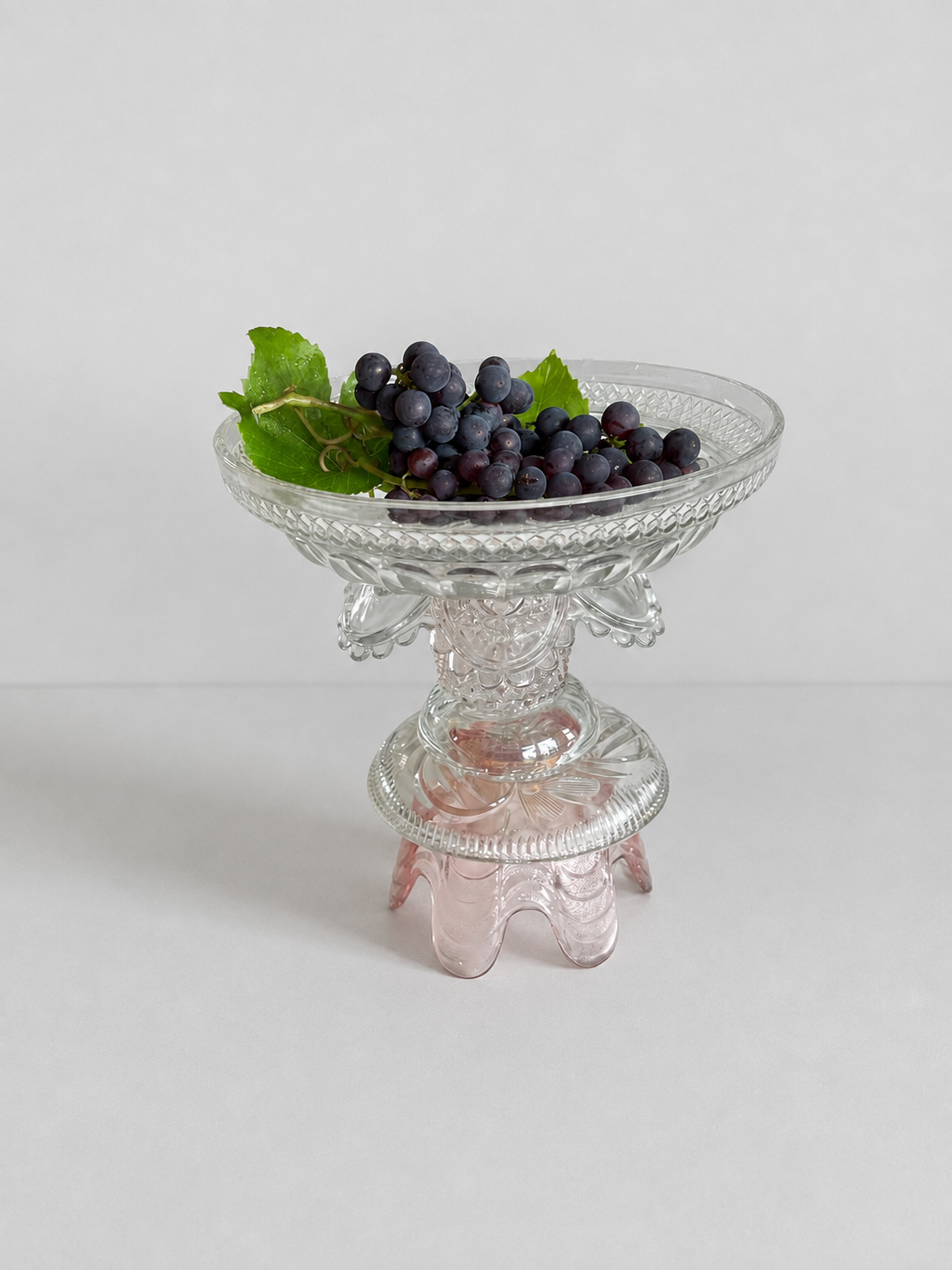 Clear and pale-pink assemblage fruit bowl holding dark grapes