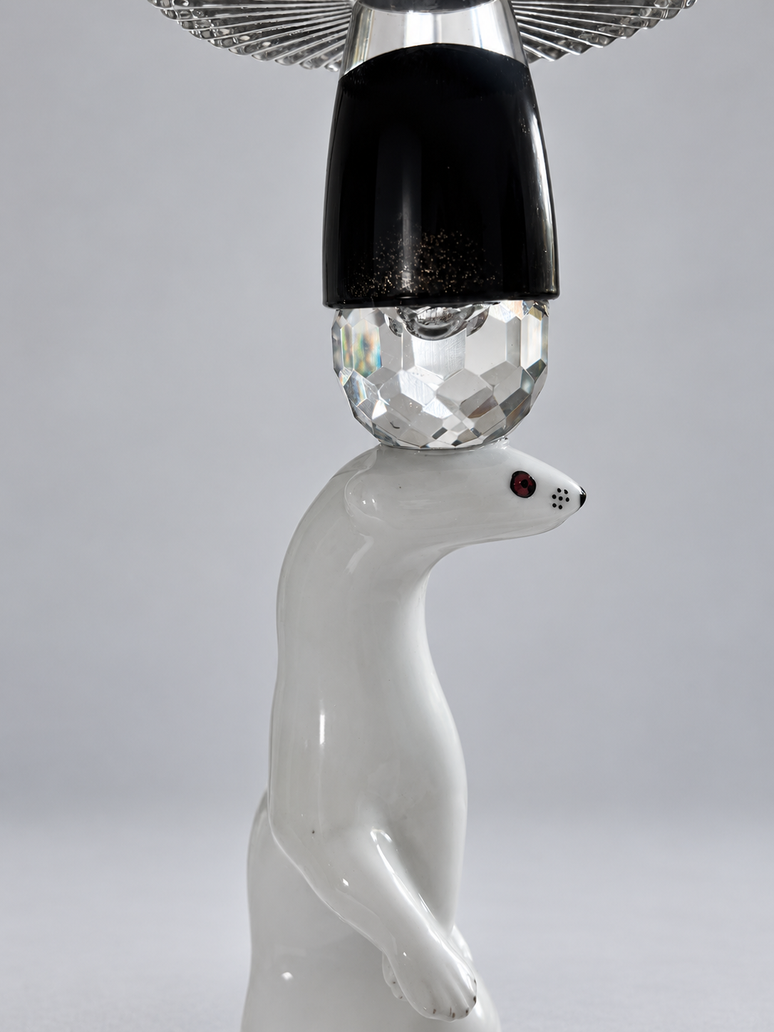 Close view of the white porcelain marten's face beneath a faceted crystal sphere