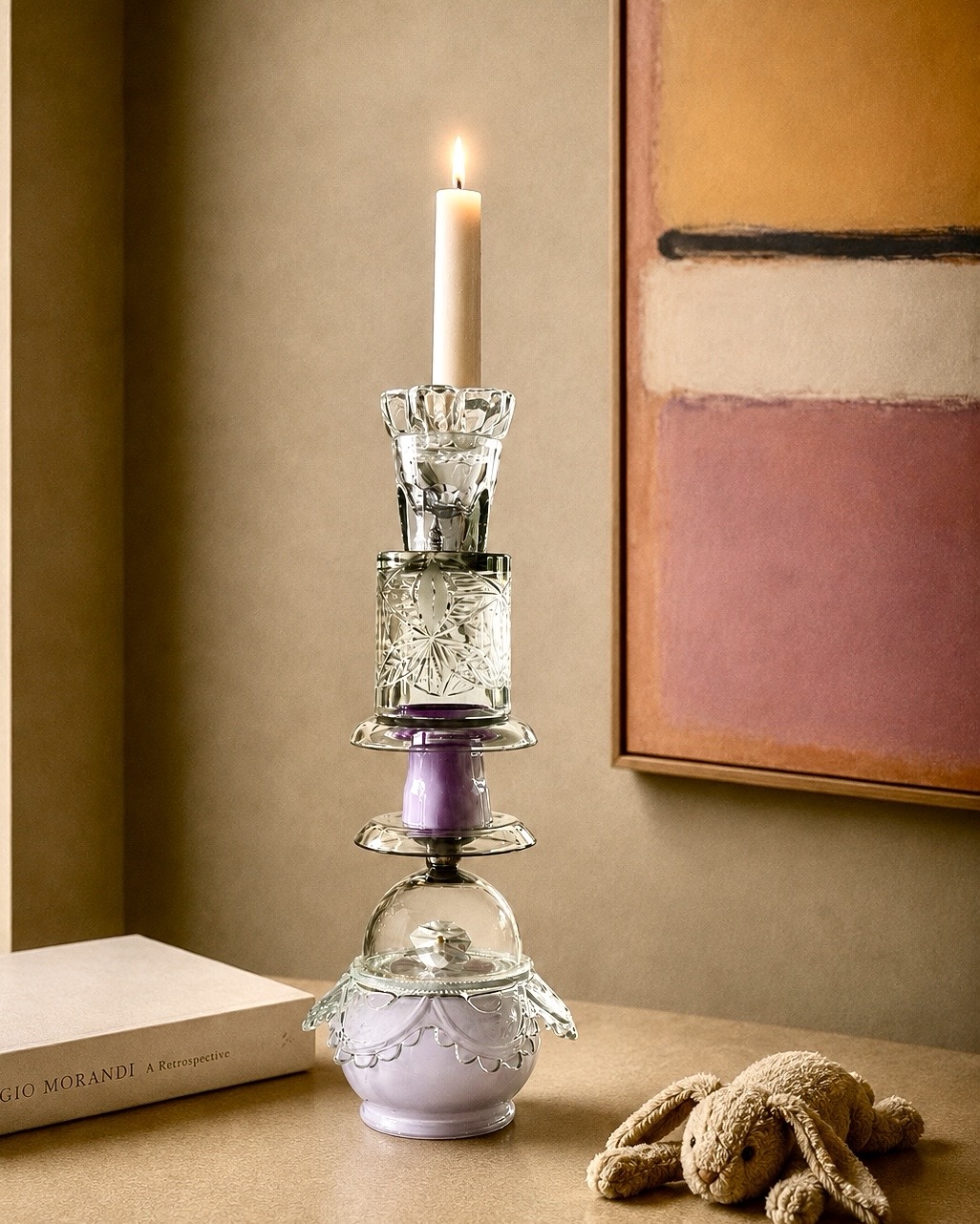 The Pantomime candleholder lit in an interior beside a book and soft toy