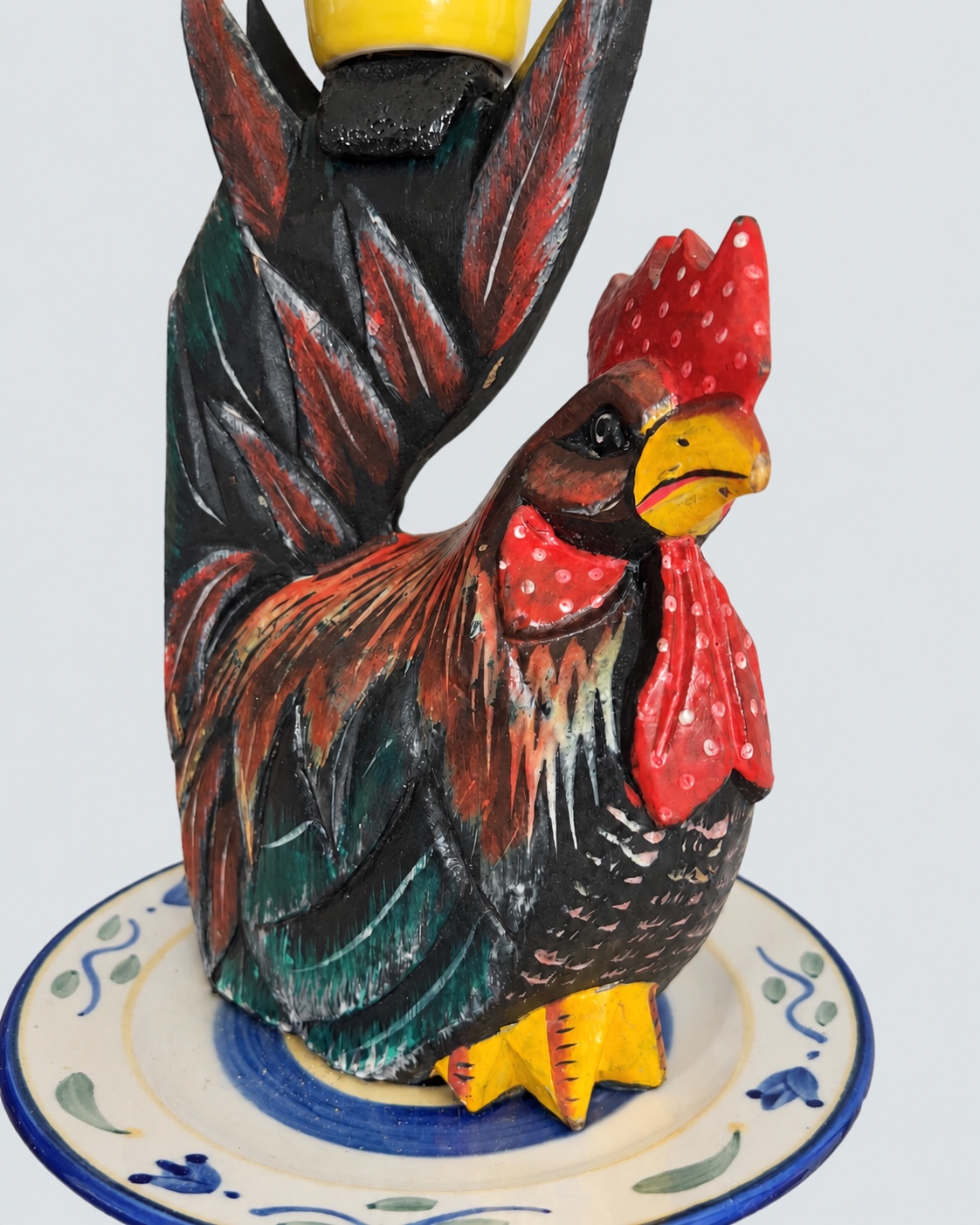 Close view of the painted wooden rooster and porcelain plate